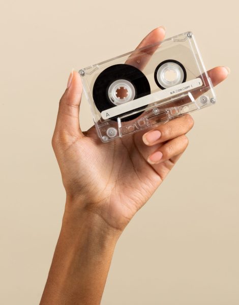 Crop anonymous African American female demonstrating vintage retro cassette tape on beige background