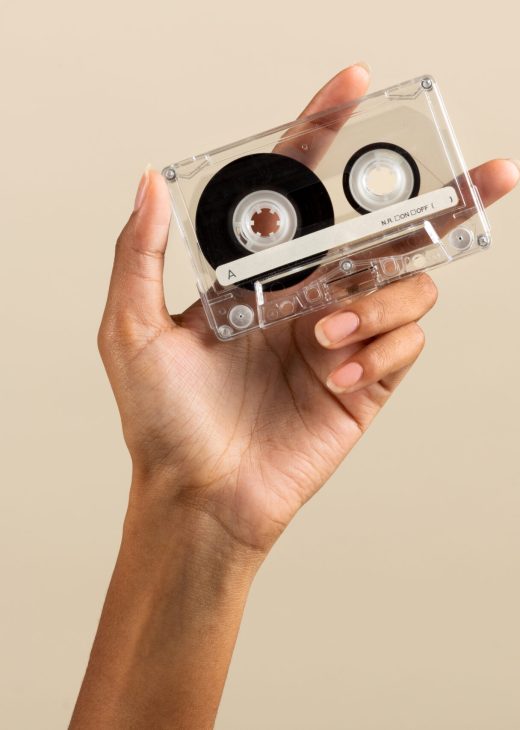 Crop anonymous African American female demonstrating vintage retro cassette tape on beige background